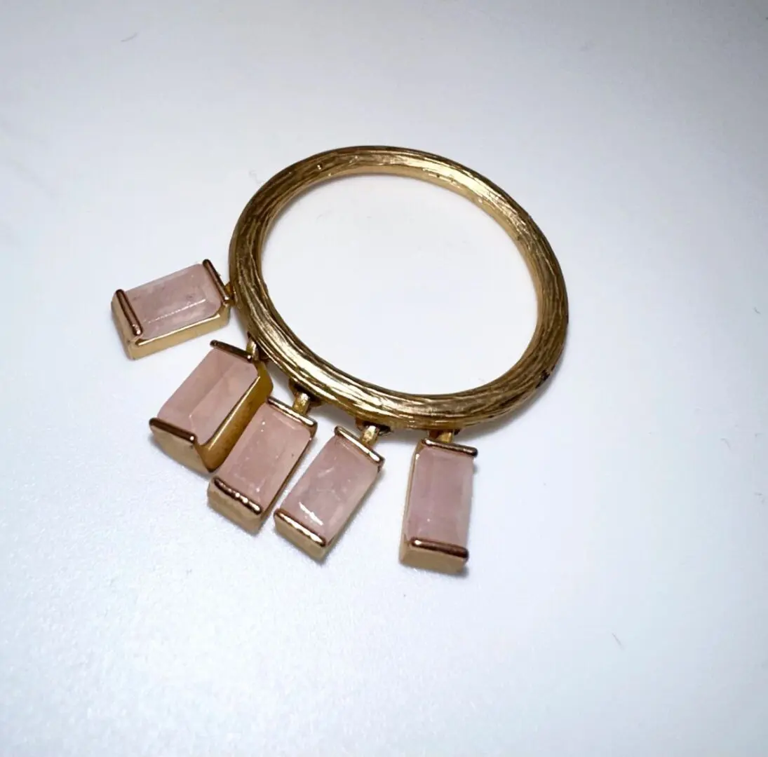 A gold ring with five pink stones dangling from it.